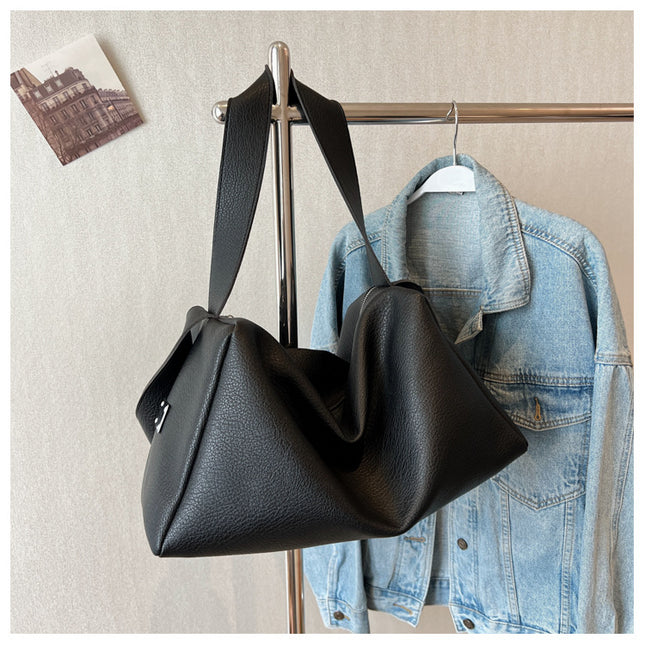 Black leather handbag hanging on a rack next to a denim jacket.