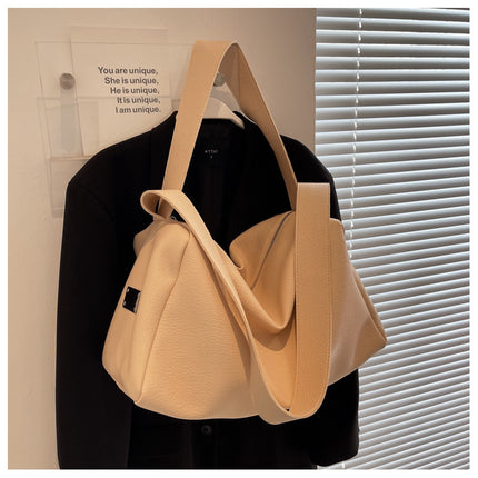 Beige handbag hanging on a black jacket against a neutral background