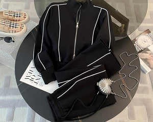 Black tracksuit with white piping on a round table with a magazine and sunglasses.
