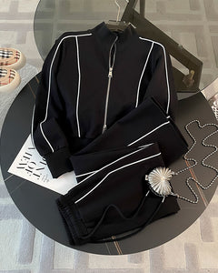 Black tracksuit with white piping on a round table with a magazine and sunglasses.