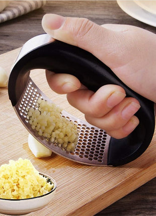 Hand using a garlic press on a wooden cutting board with minced garlic and whole garlic cloves.
