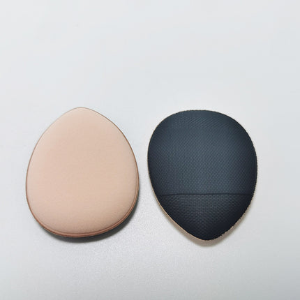 Two makeup sponges, one beige and one black textured, on a light gray background.