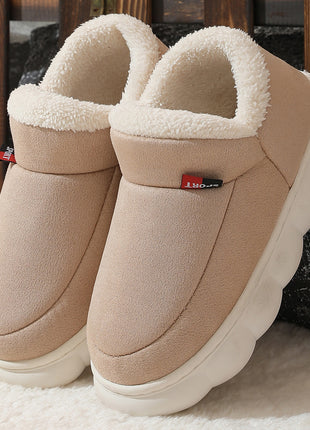 Pair of beige slippers with white fur lining on a soft surface.