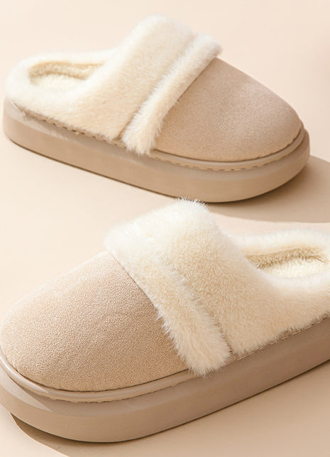 Pair of beige slippers with white fur trim on a beige background
