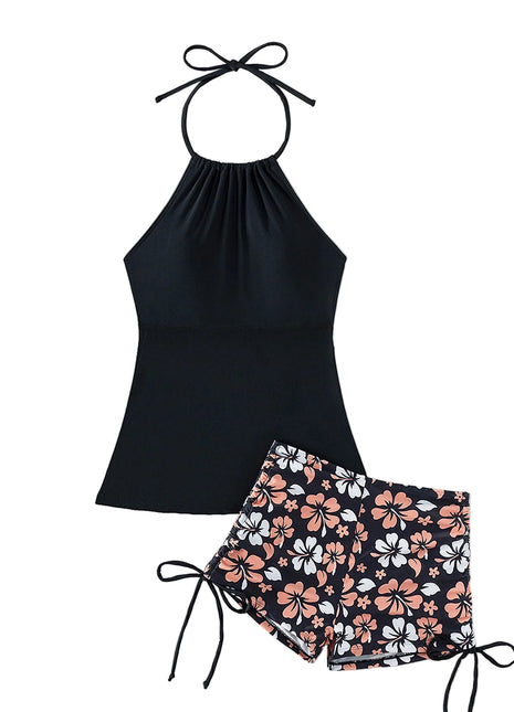 Black halter top and floral shorts set with a straw hat and sunglasses on a light background
