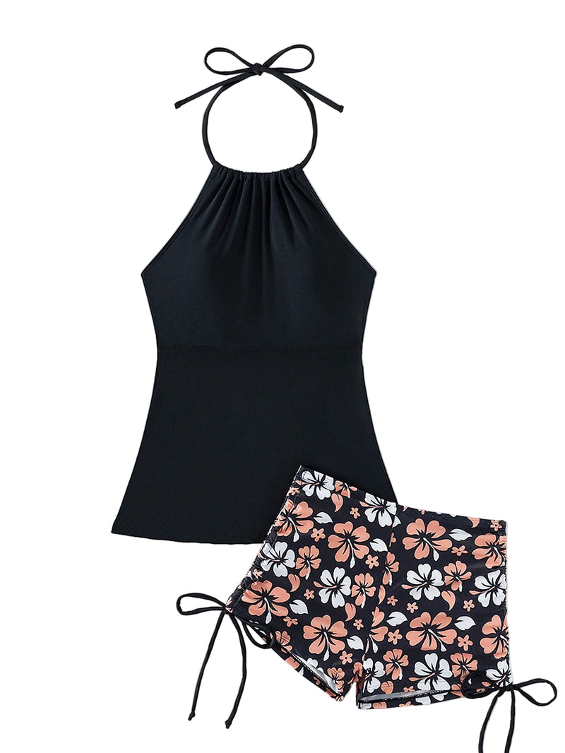 Black halter top and floral shorts set with a straw hat and sunglasses on a light background