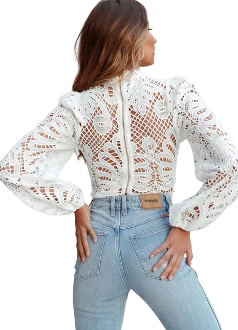 Woman wearing a white lace top and light blue jeans with a plant in the background