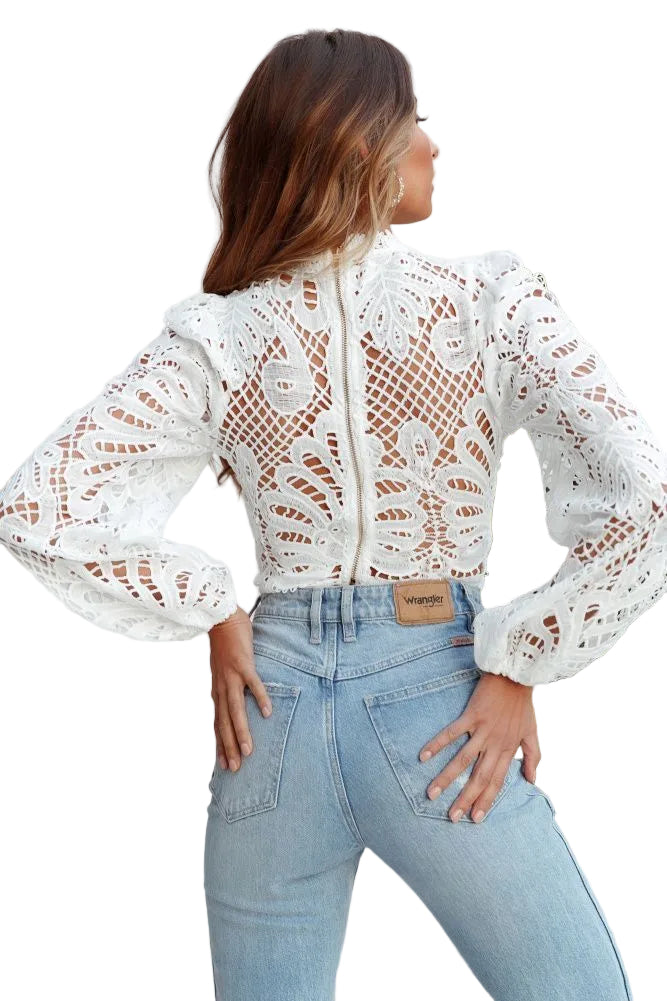 Woman wearing a white lace top and light blue jeans with a plant in the background