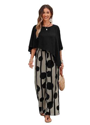 Woman wearing a black top and polka dot pants standing in front of a white brick wall.