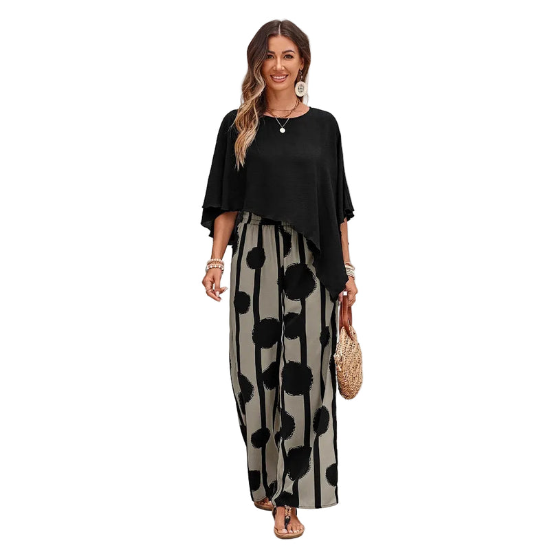 Woman wearing a black top and polka dot pants standing in front of a white brick wall.