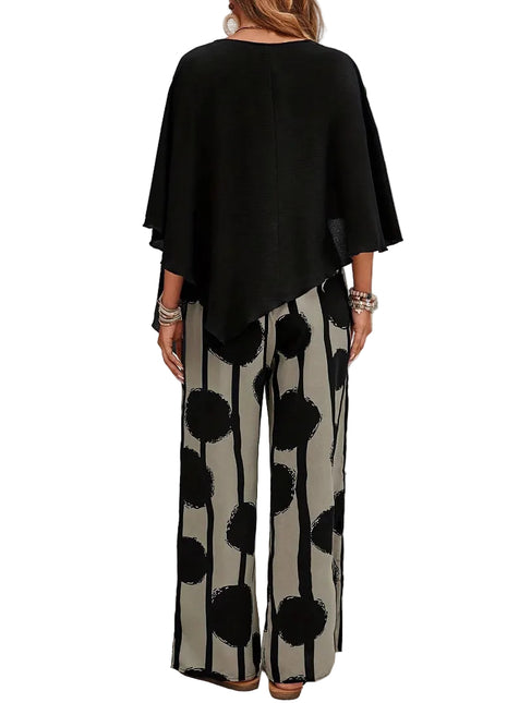 Woman wearing a black top and patterned pants standing in front of a white brick wall.