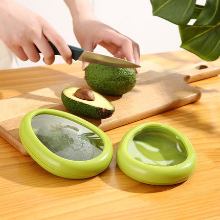 Person cutting an avocado on a wooden board with two green avocado holders in the foreground.
