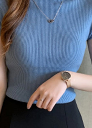 Person wearing a blue ribbed top and black pants with a neutral background