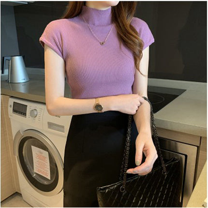 Person wearing a purple ribbed top and black pants in a kitchen.